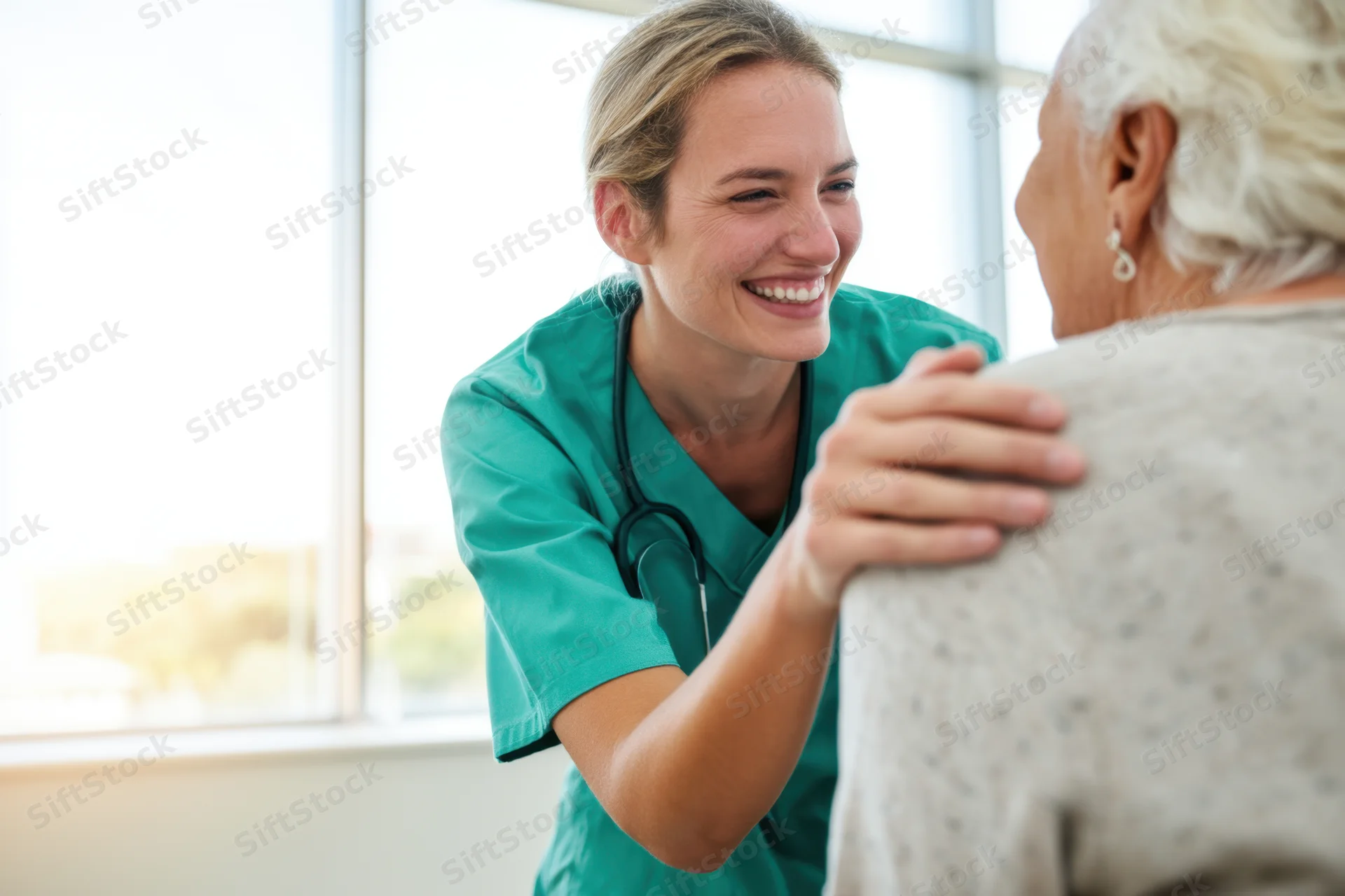 Nurse in teal scrubs smiling and placing hand on senior patient’s shoulder in clinic