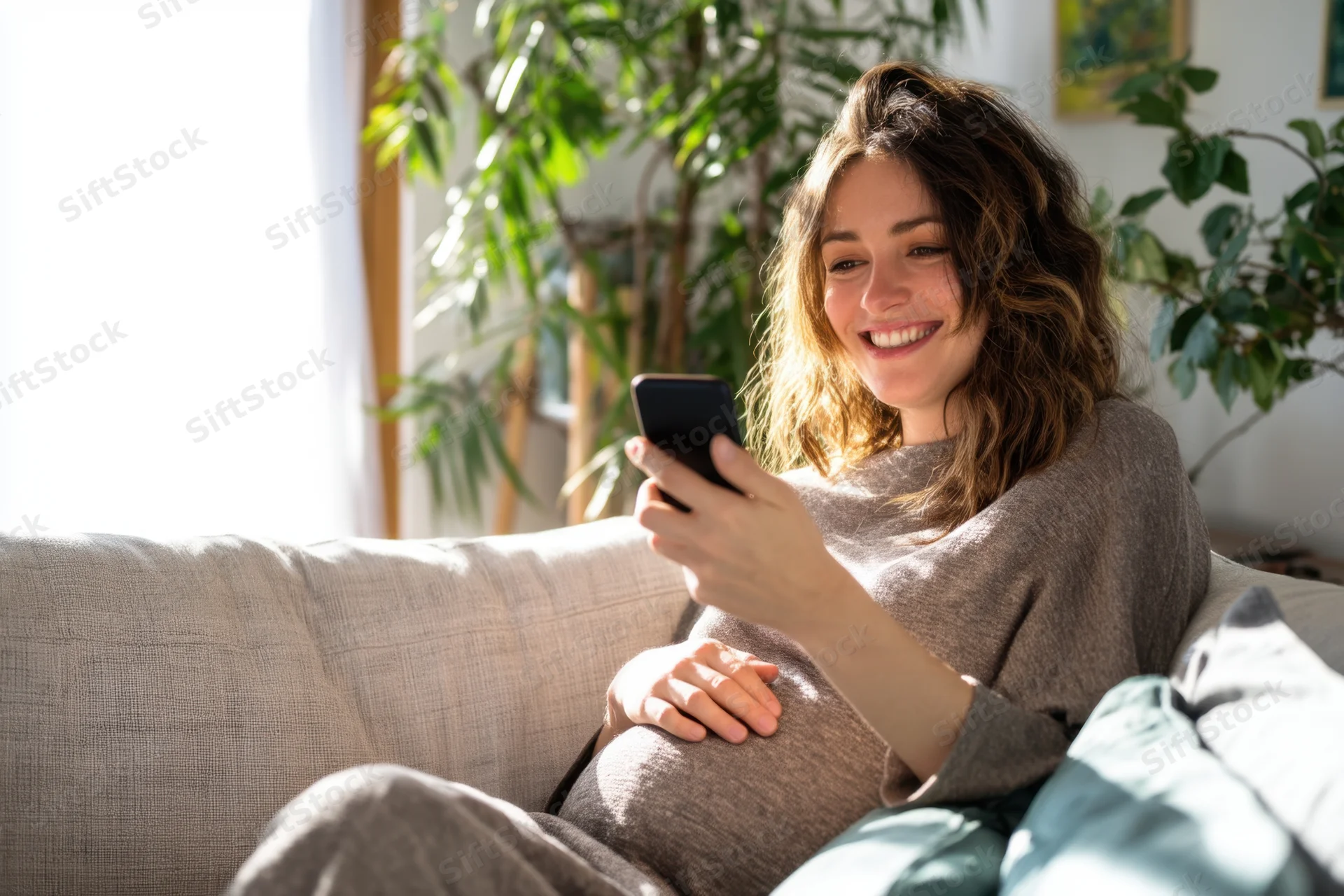 Pregnant woman smiling while using smartphone on couch at home