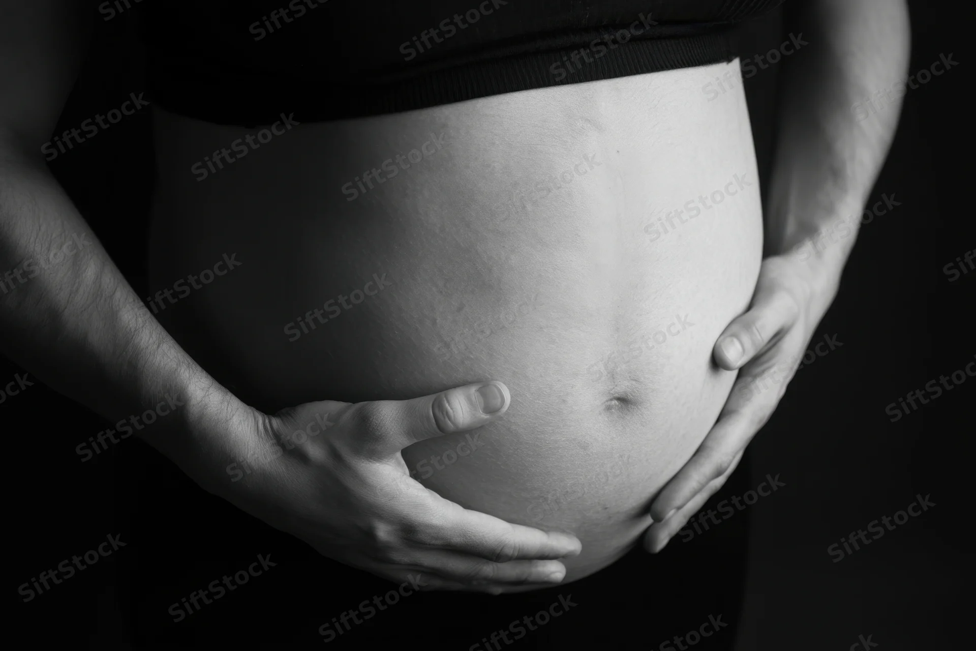 Pregnant woman cradling her belly with hands in close-up view