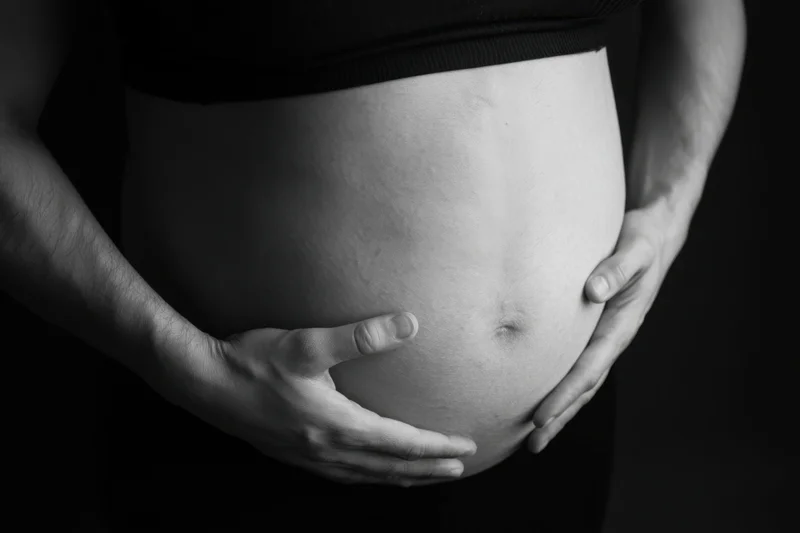 Pregnant woman cradling her belly with hands in close-up view