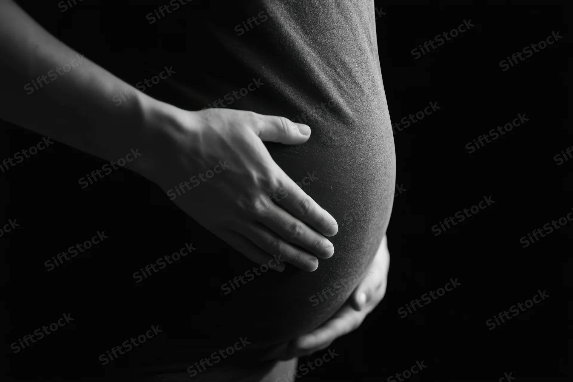 Pregnant woman cradling her belly against a dark background