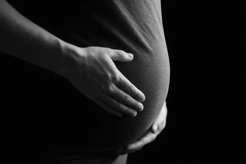Pregnant woman cradling her belly against a dark background