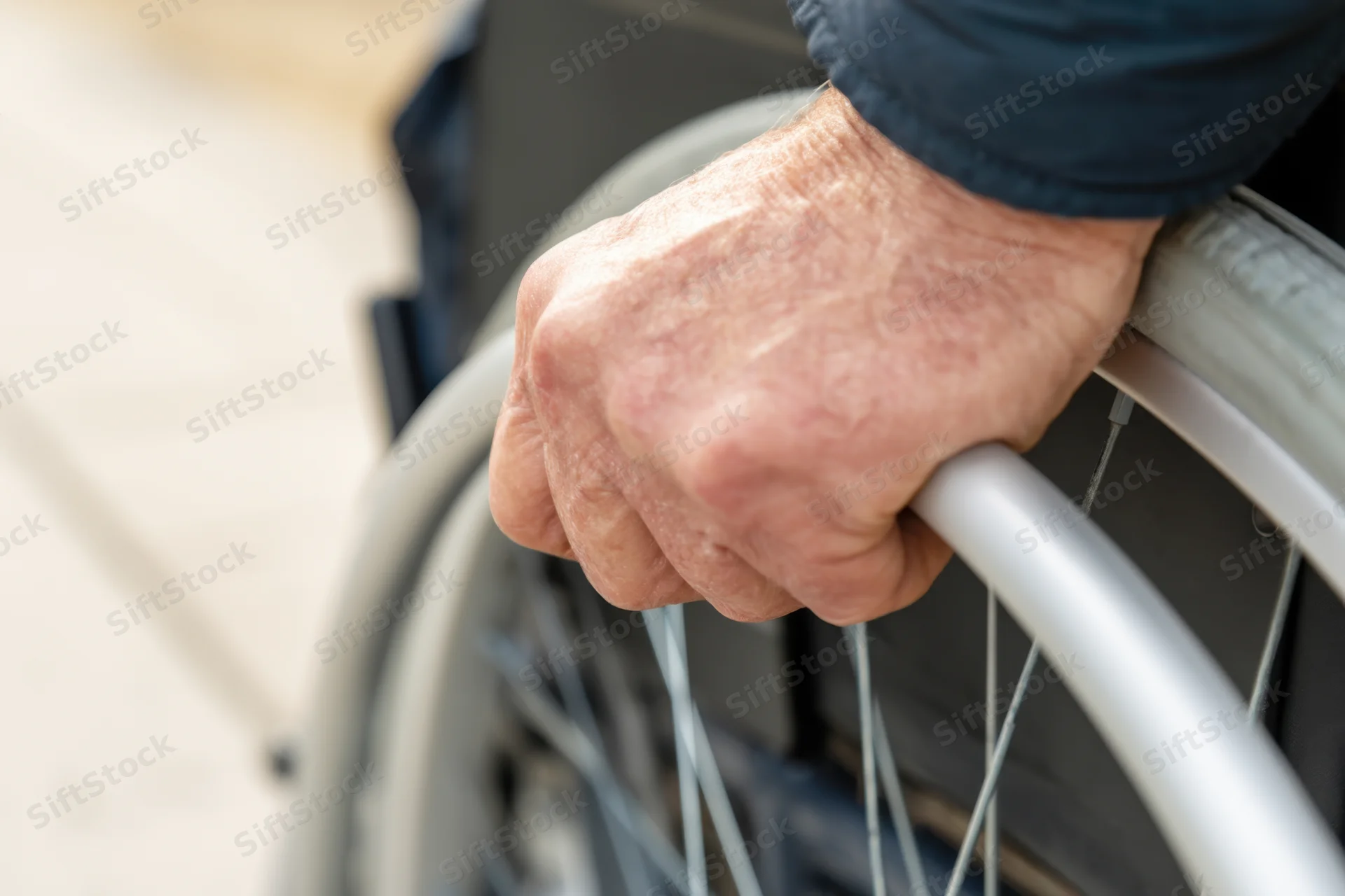 Close-up of an elderly person's hand gripping the rim of a wheelchair outdoors