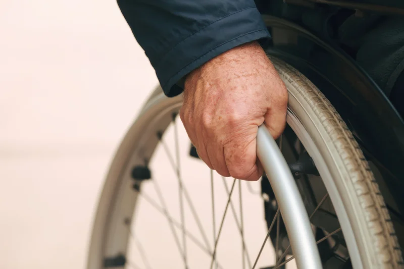 Close-up of a senior man's hand gripping the wheel of a wheelchair