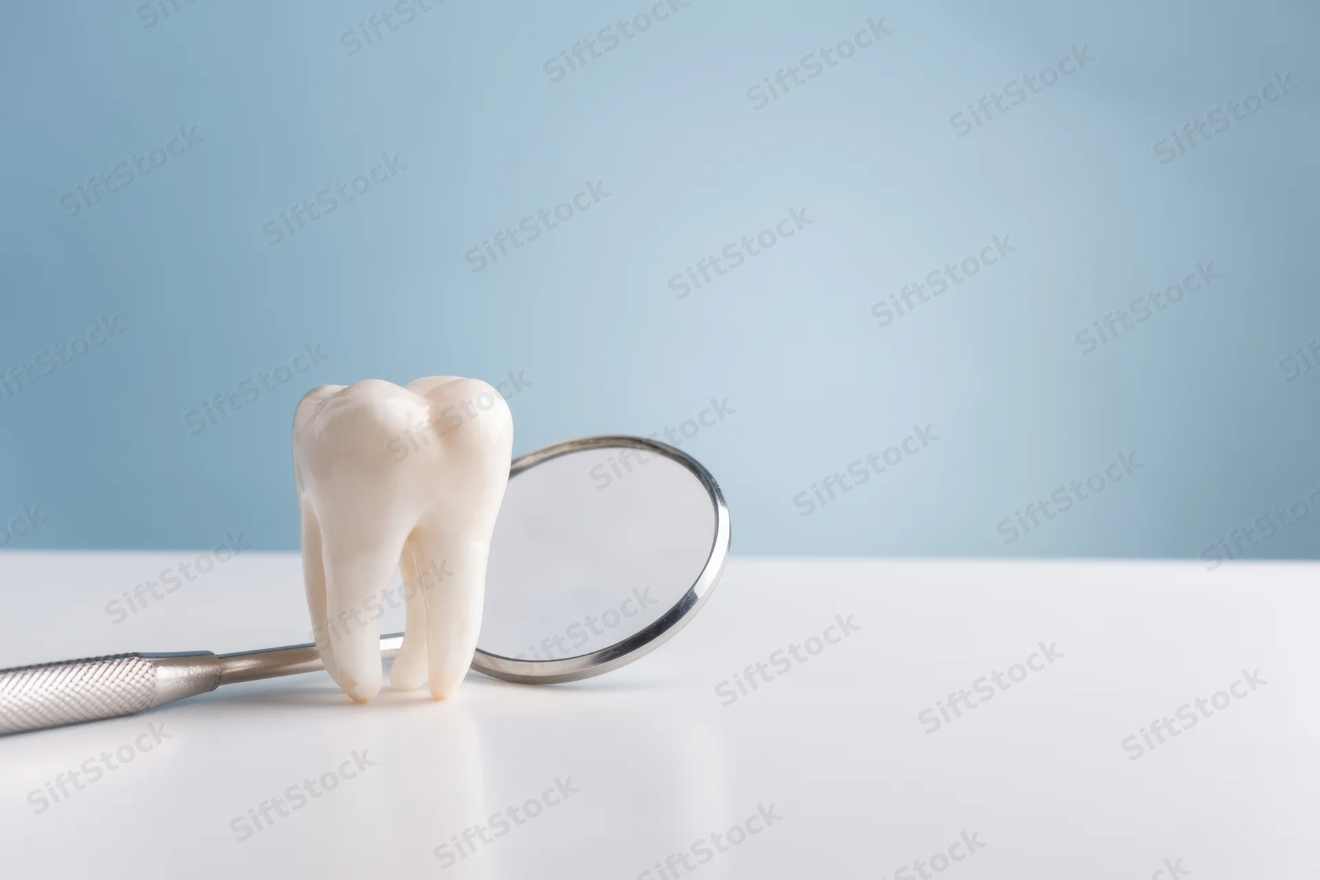 A white tooth model resting beside a dental mirror on a clean surface with blue background
