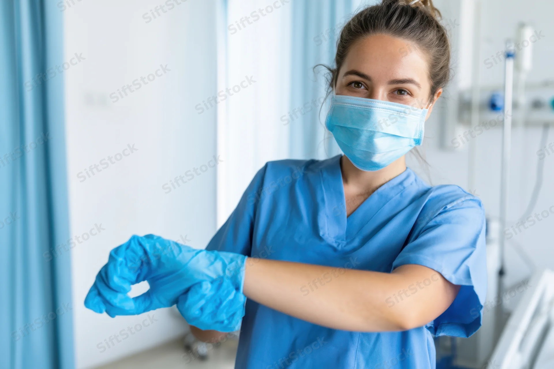 Nurse in blue scrubs putting on gloves in a hospital room