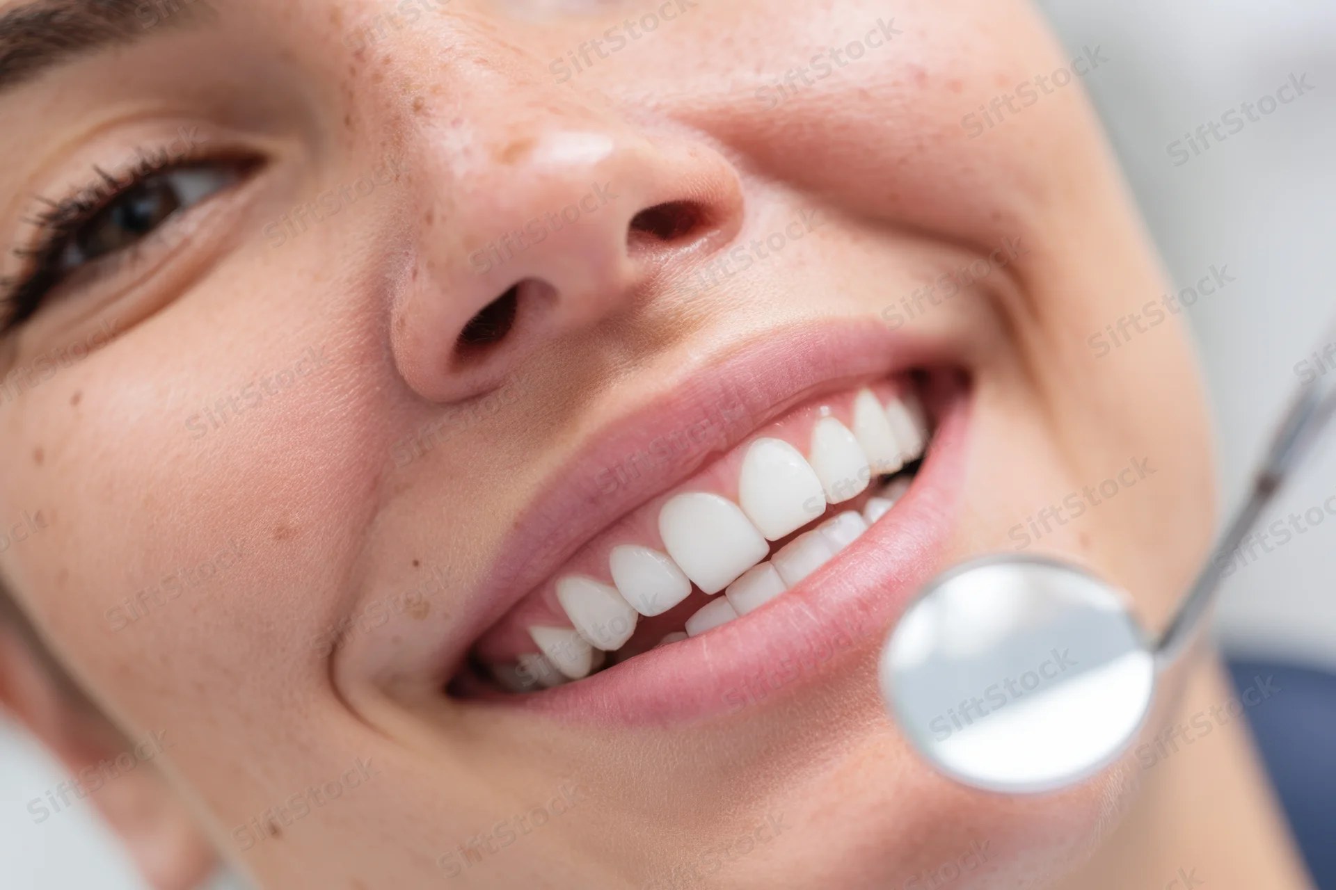 Closeup of a smiling woman with dental mirror near her teeth in a clinic