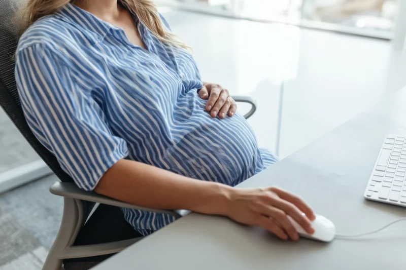 Pregnant woman sitting at office desk using computer mouse while resting hand on belly