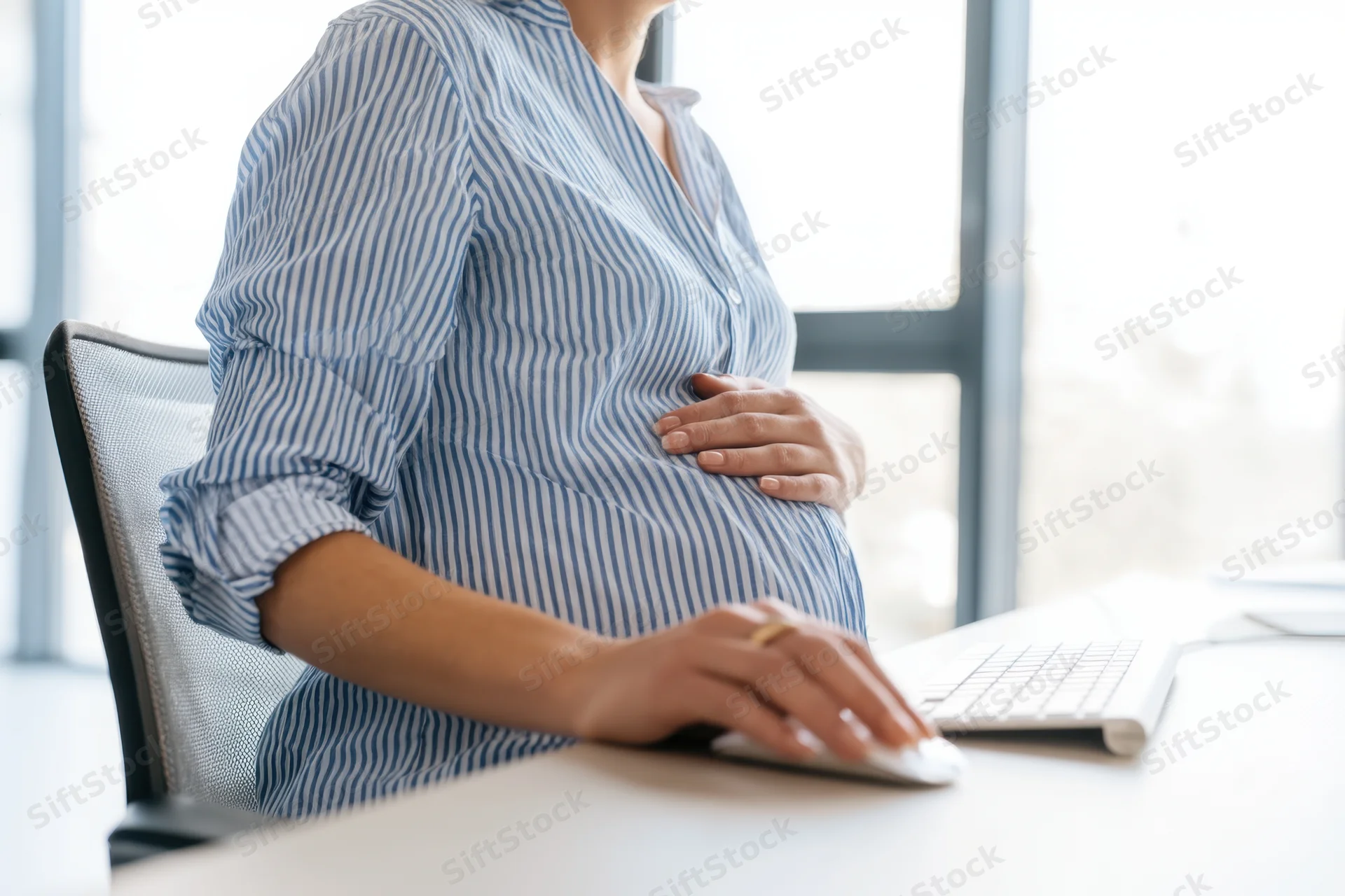 Pregnant woman sitting at office desk using computer mouse while resting hand on belly