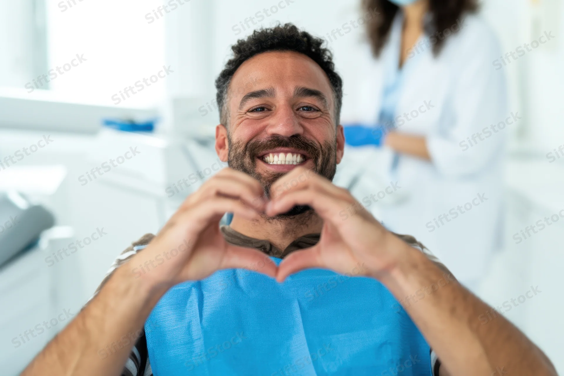 Smiling man making heart shape with hands in dental clinic