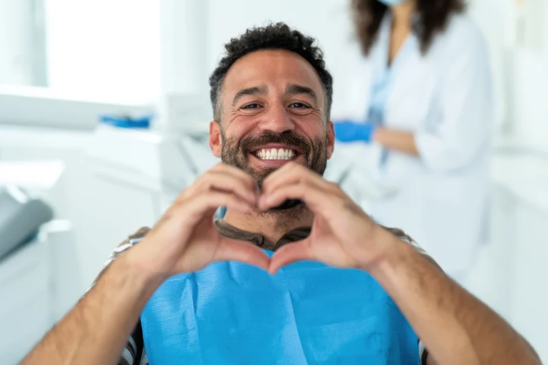 Smiling man making heart shape with hands in dental clinic