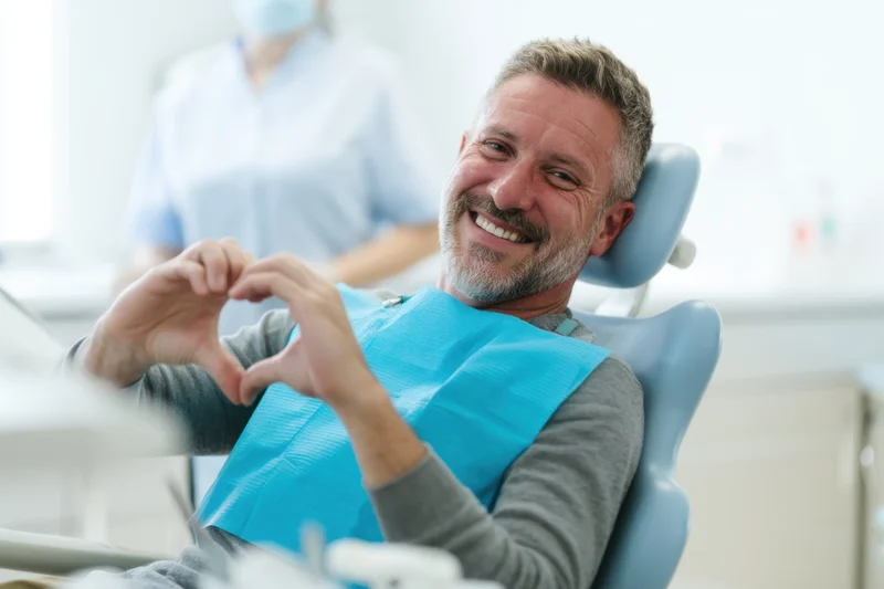 Smiling man in dental chair making heart shape with hands during appointment
