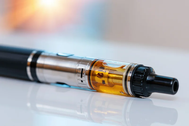 Black and silver vape pen mod lying horizontally on a reflective white surface