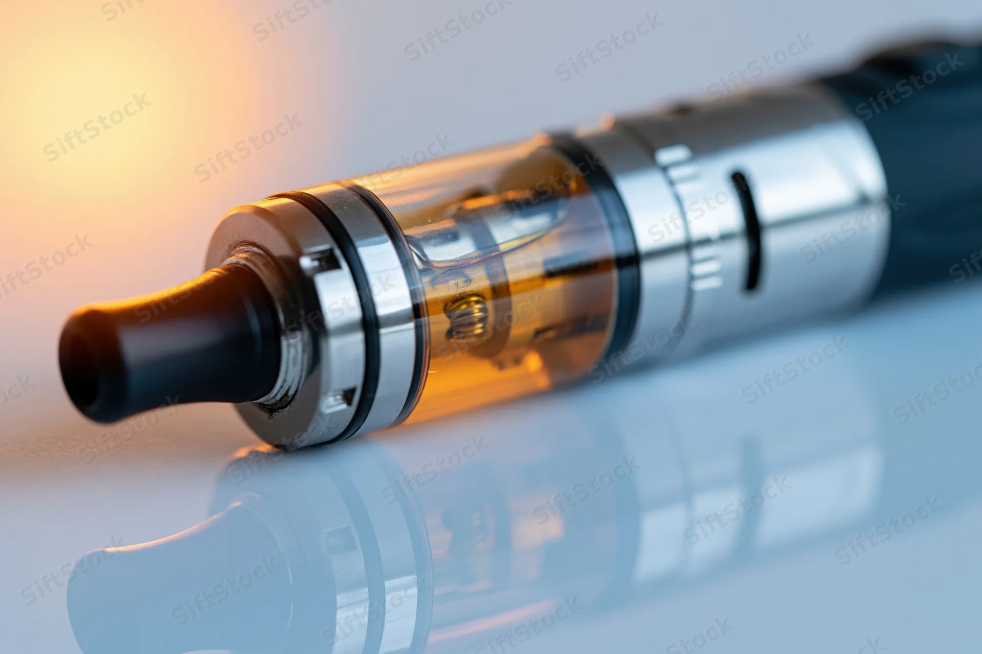 Black and silver vape pen mod lying horizontally on a reflective surface with visible glass tank and coil inside