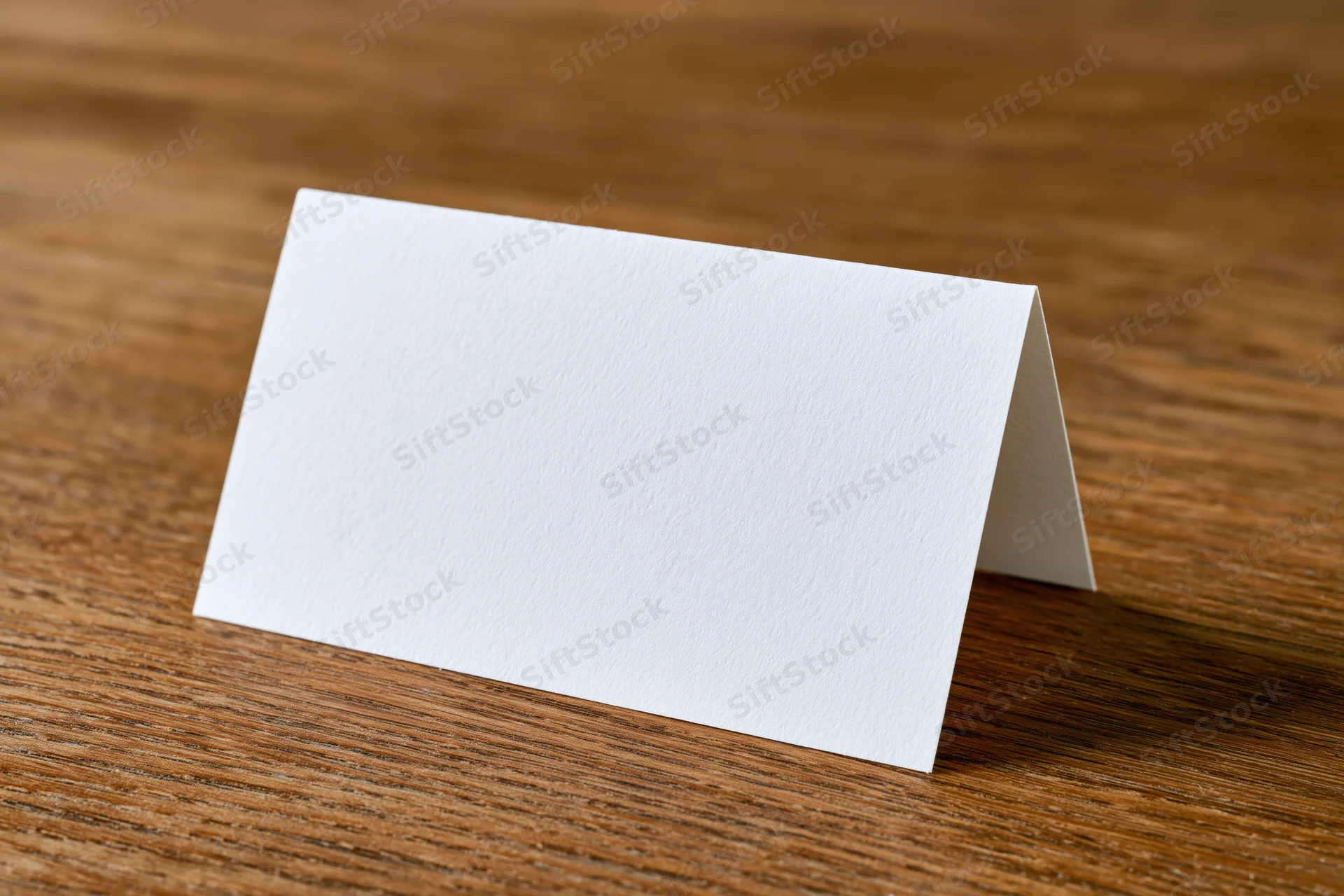 Blank white folded tent card standing upright on warm oak tabletop
