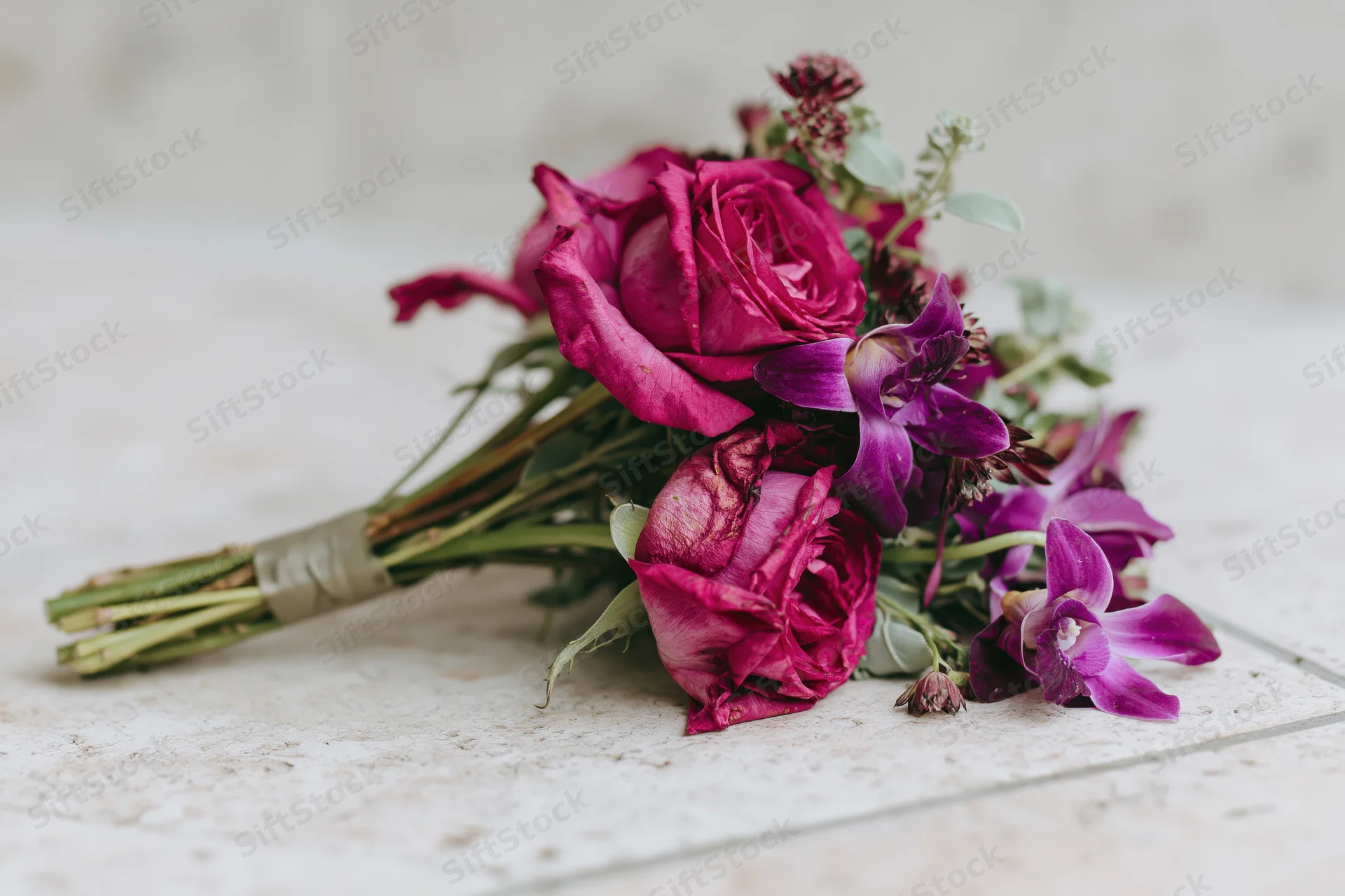 Bridal bouquet of pink roses and purple orchids resting on a tiled floor