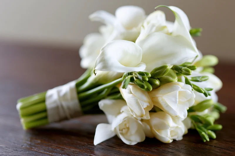 Bridal bouquet of white calla lilies and freesias arranged on a wooden table