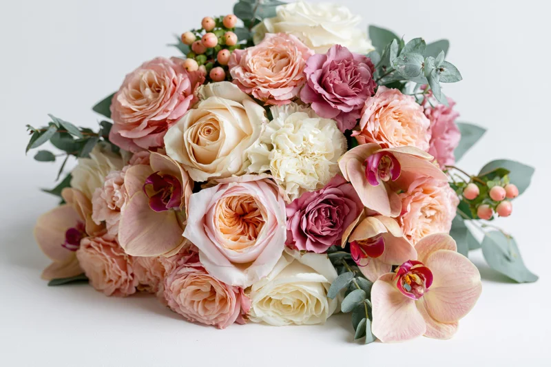 Bridal bouquet of pink and white roses with orchids and eucalyptus resting on white surface