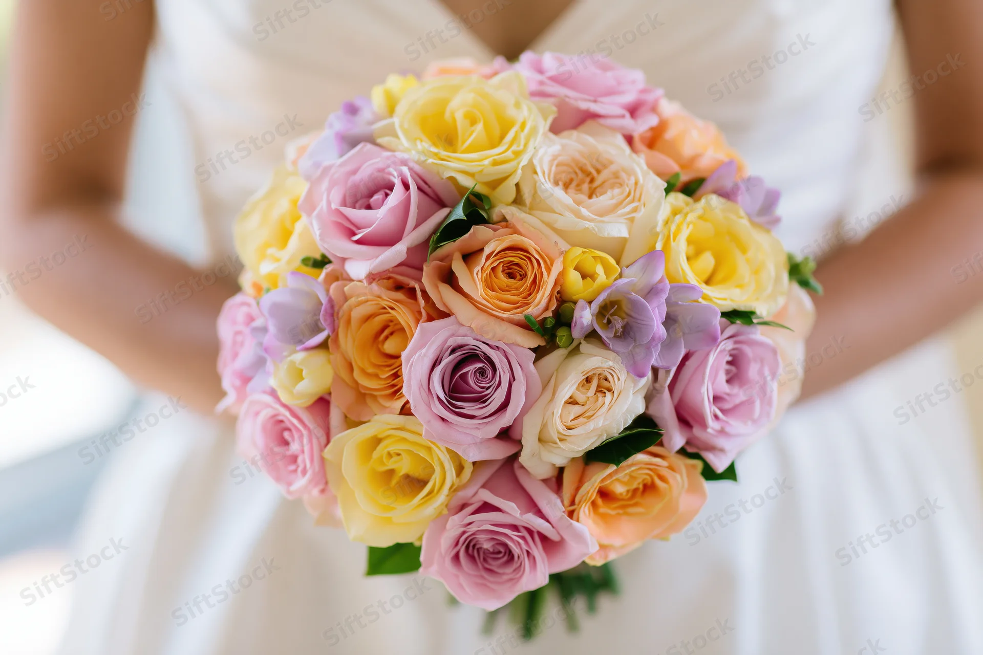 Bride holding a round bouquet of pastel roses in a white dress