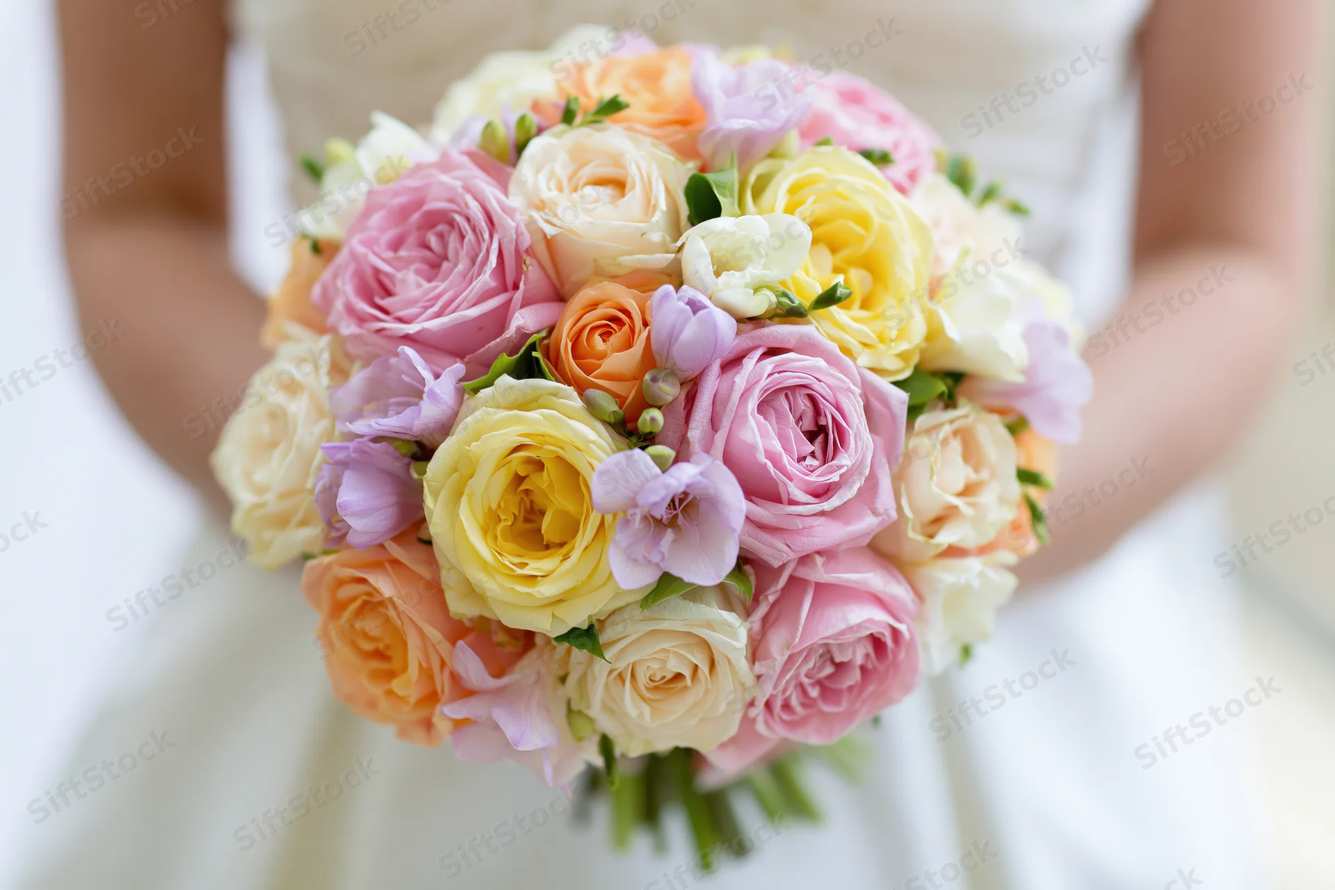 Bride holding a round bouquet of pink, yellow, orange and white roses