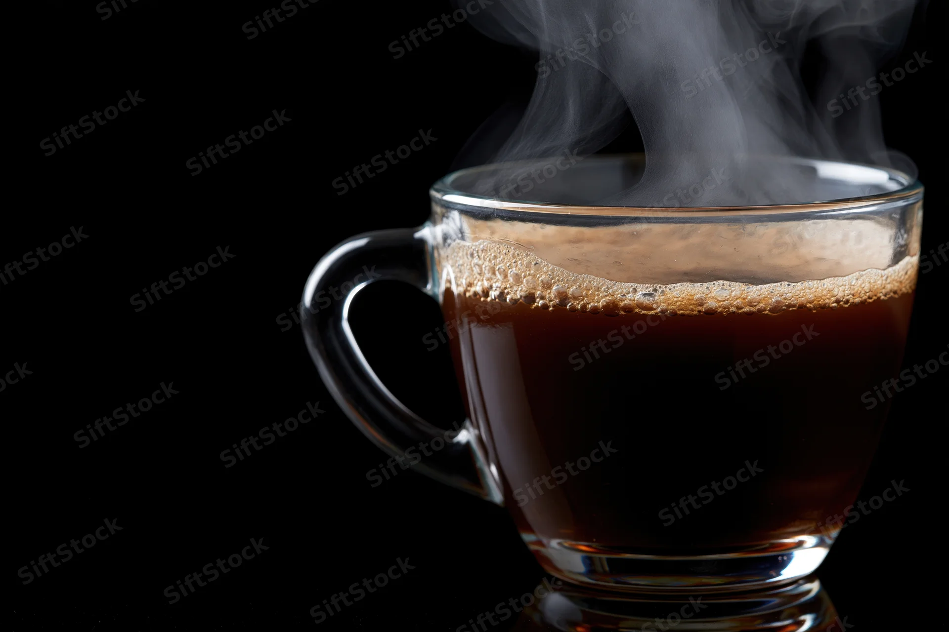 Hot black coffee steaming in a clear glass cup against black background