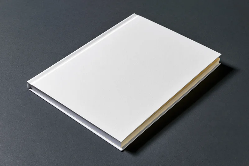 Closed softcover booklet with blank white cover on dark surface