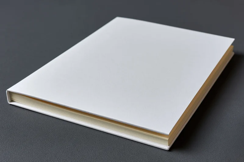 Closed softcover booklet with blank white cover resting on dark surface
