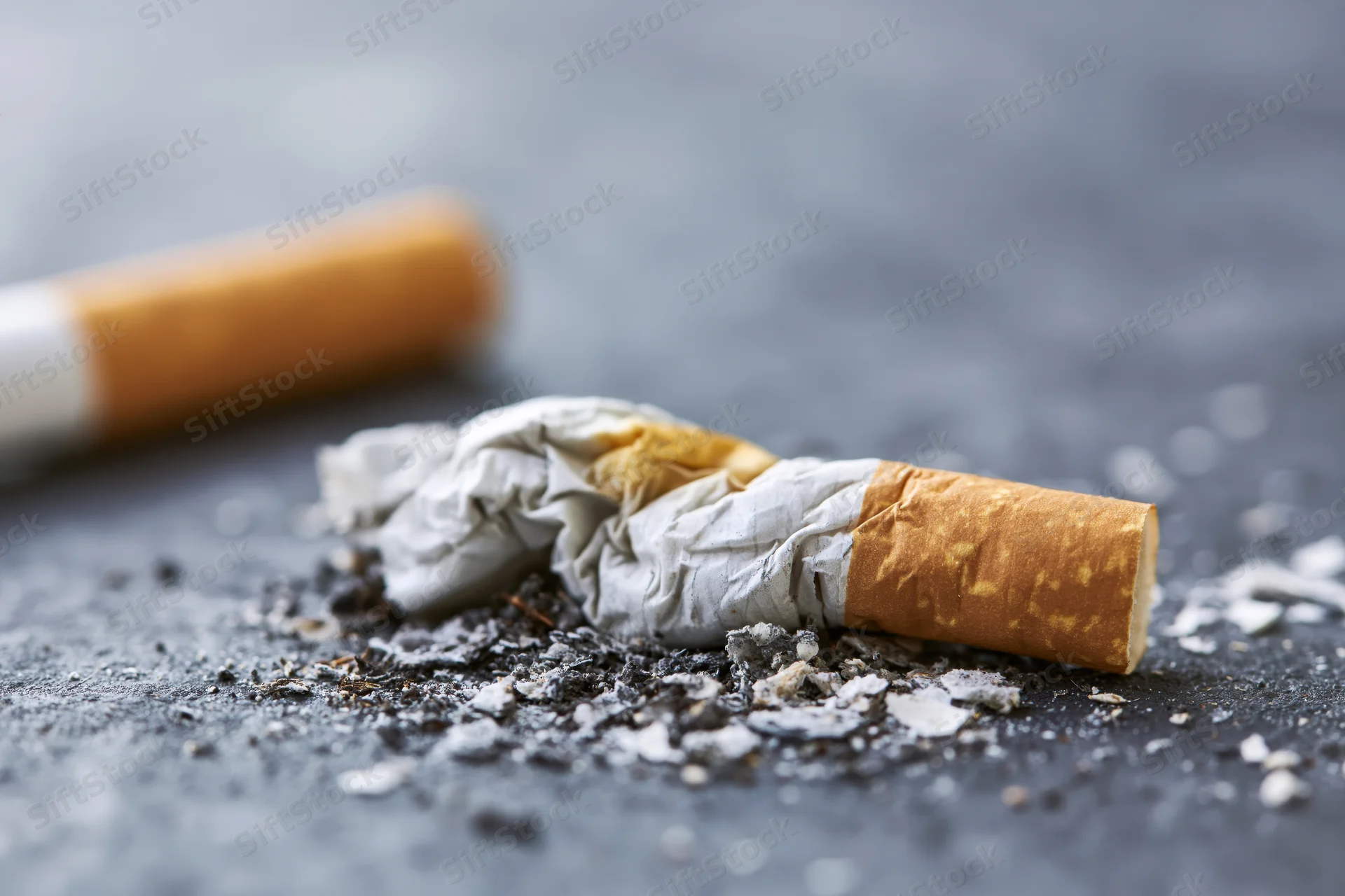 Crushed cigarette butt with ash on dark textured surface