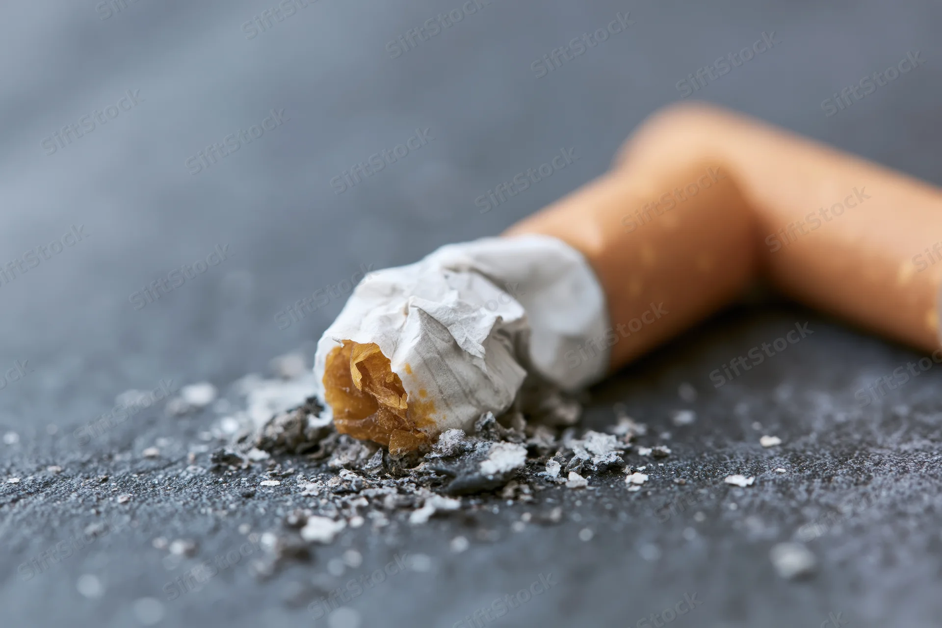Crushed cigarette butt with ash on dark grey textured surface