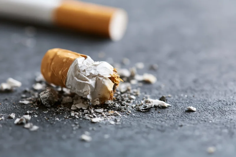 Crushed cigarette butt with ash on dark textured surface