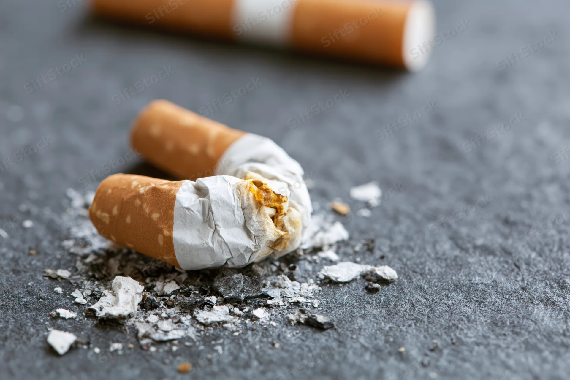 Crushed cigarette butt with ash on dark grey textured surface