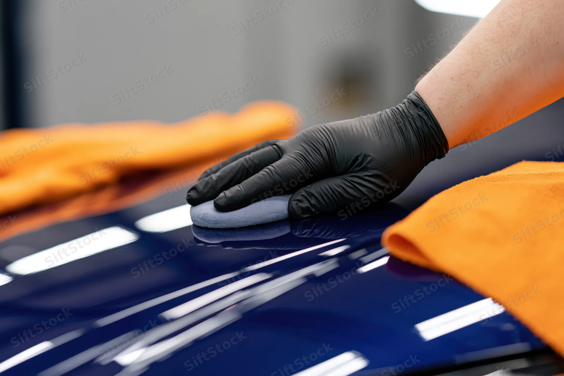 A detailer’s gloved hand applying polish to a glossy blue car surface with a gray applicator pad