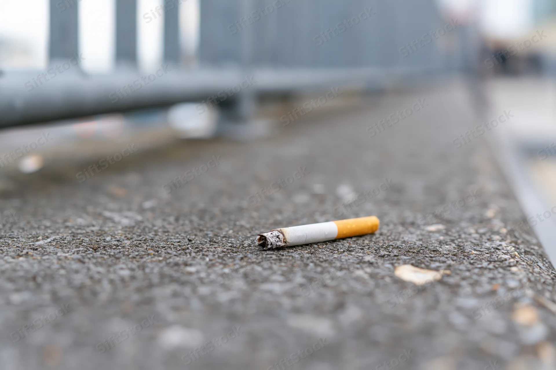 Discarded cigarette butt lying on rough gray concrete pavement