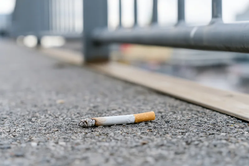 Discarded cigarette butt lying on rough gray concrete pavement near metal railing