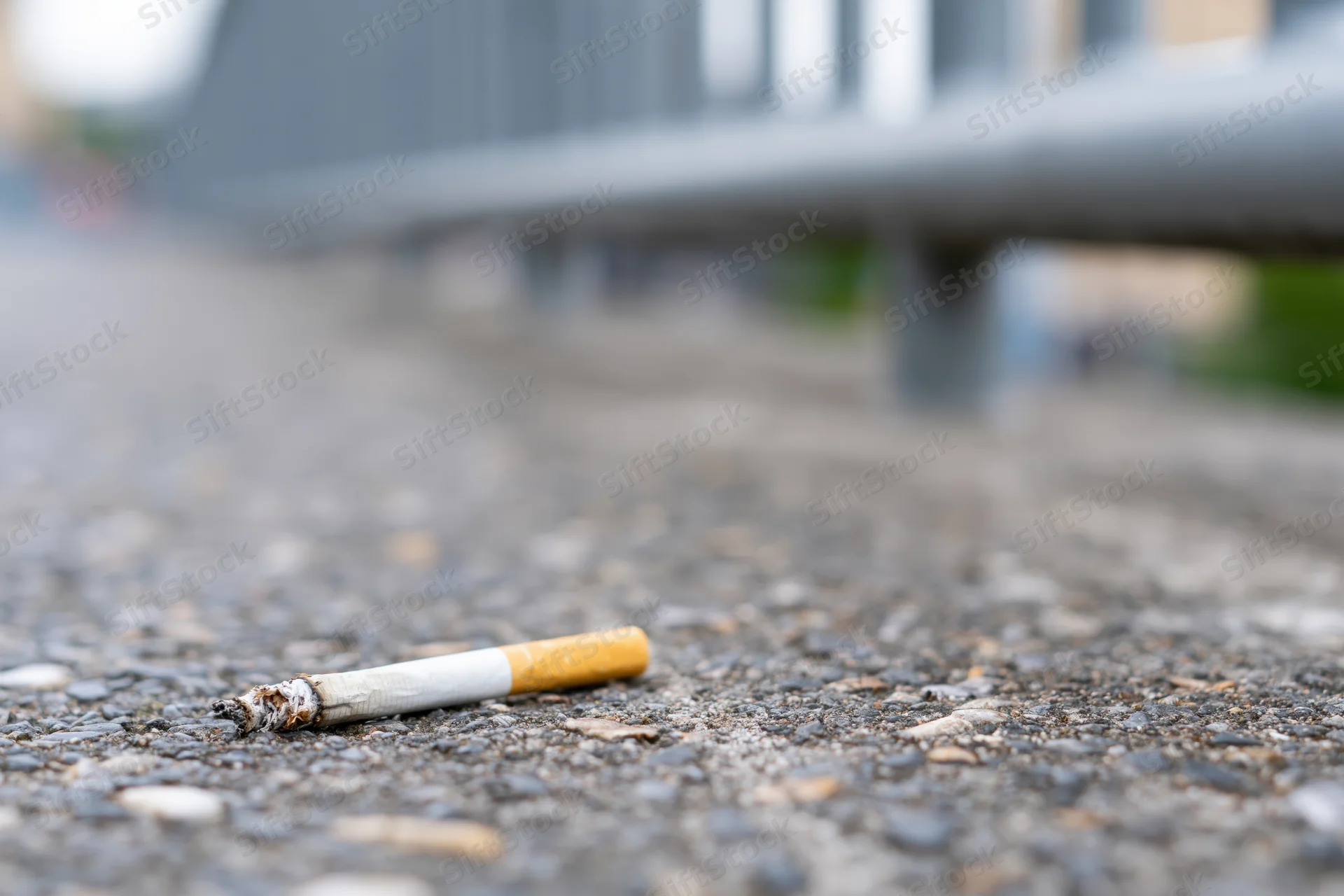 Discarded cigarette butt lying on rough gray concrete pavement
