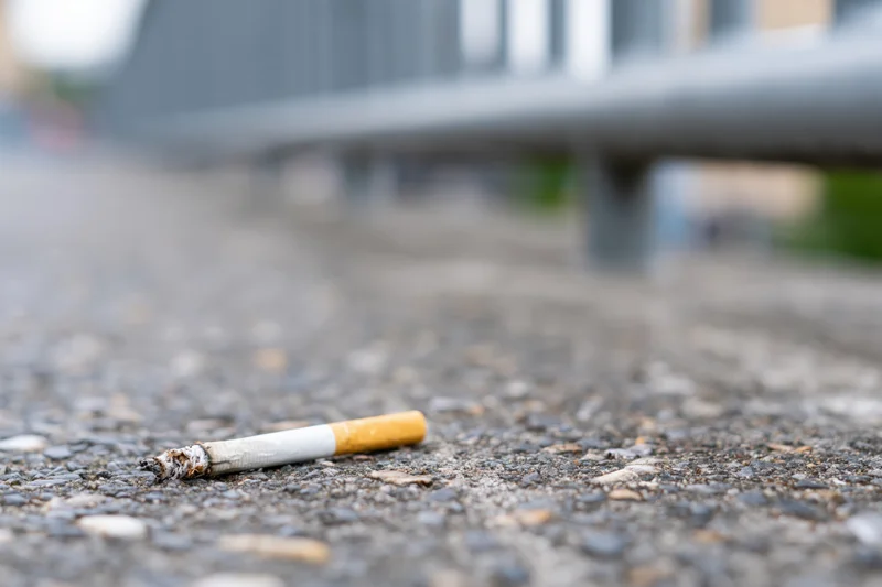 Discarded cigarette butt lying on rough gray concrete pavement