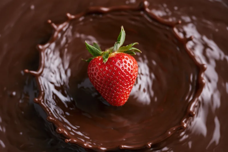 Fresh strawberry with green leaves landing in liquid chocolate, creating a splash and ripple effect
