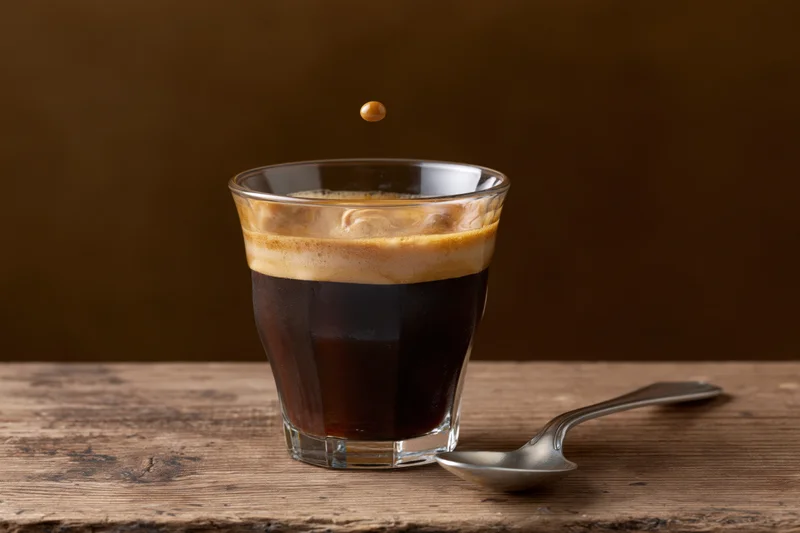 Espresso in a glass cup with crema and a spoon on a wooden table