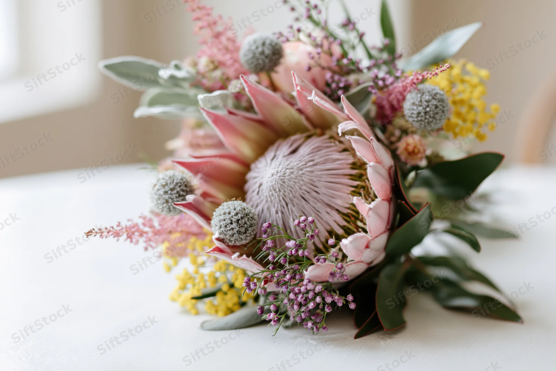 King protea at center of mixed wildflower bouquet on white table surface