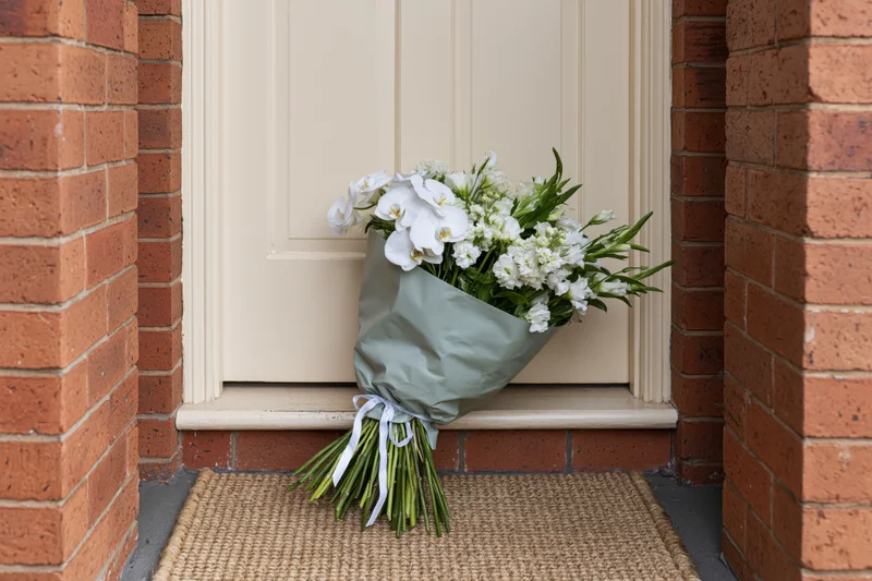 Wrapped white flower bouquet resting on doormat at brick house entrance