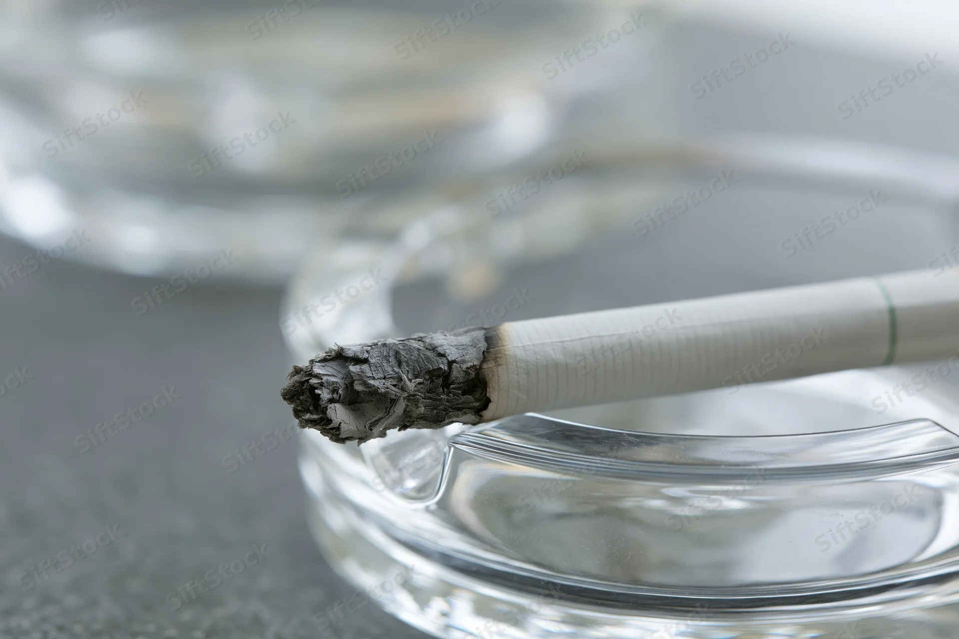 Lit cigarette with long gray ash resting on glass ashtray