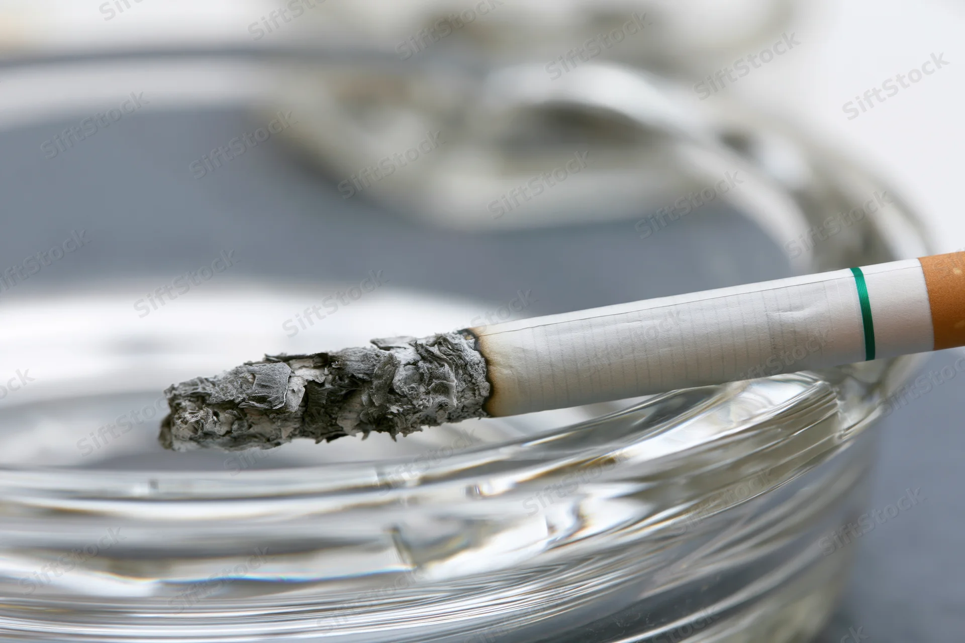Lit cigarette with long gray ash resting across grooved glass ashtray