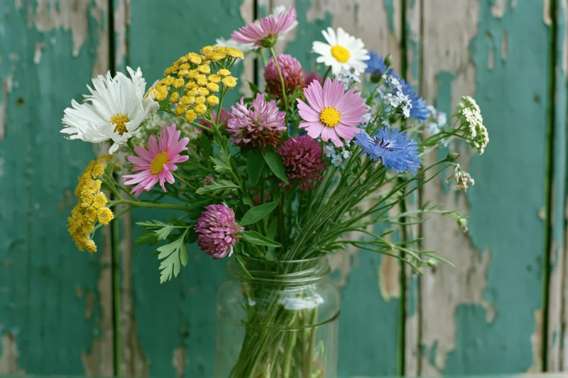 Wildflower bouquet in a clear glass jar against a weathered teal wooden wall