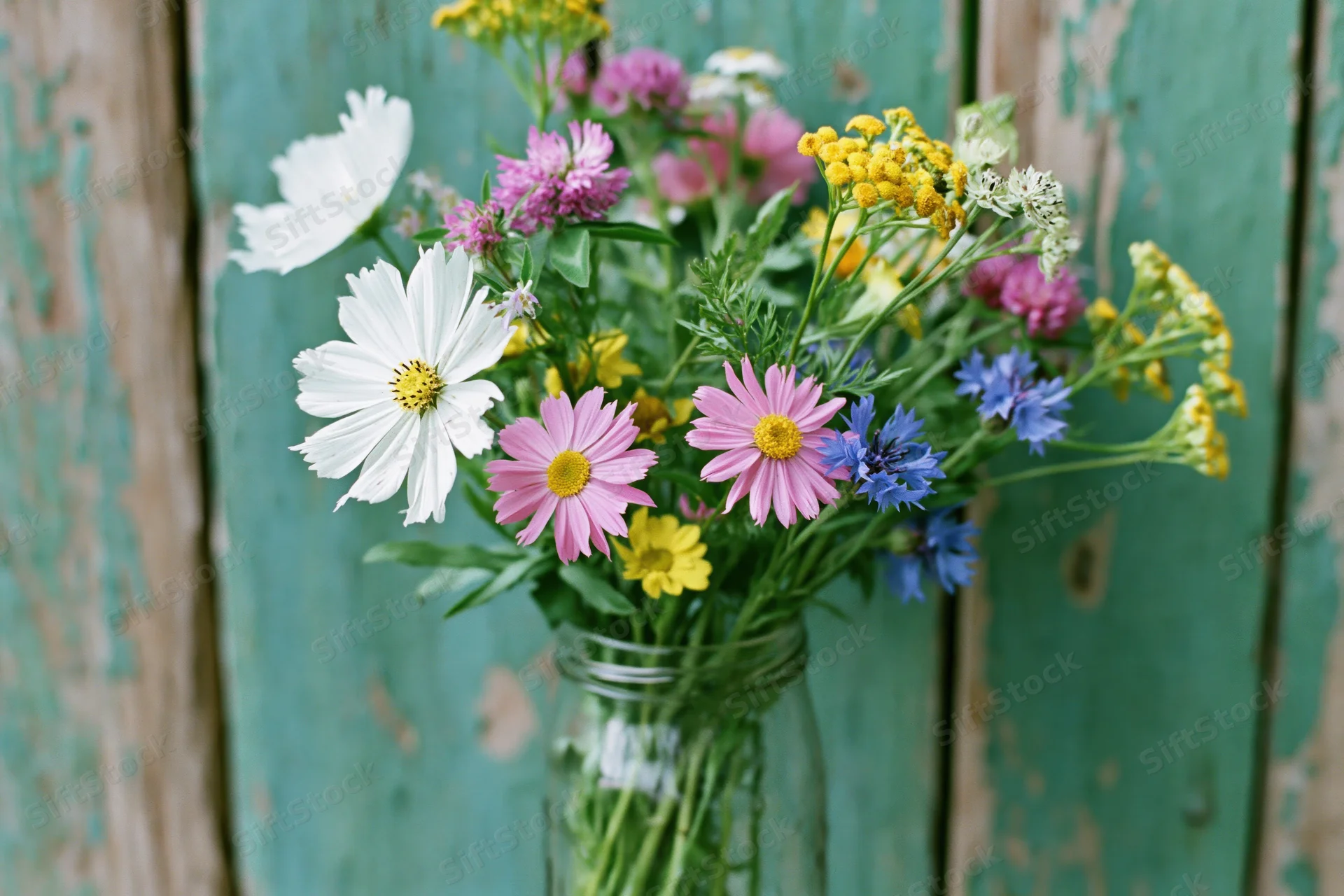 Loose wildflower bouquet in a clear glass jar against weathered teal wood