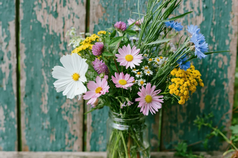 Loose wildflower bouquet in a clear glass jar against a weathered teal wooden fence