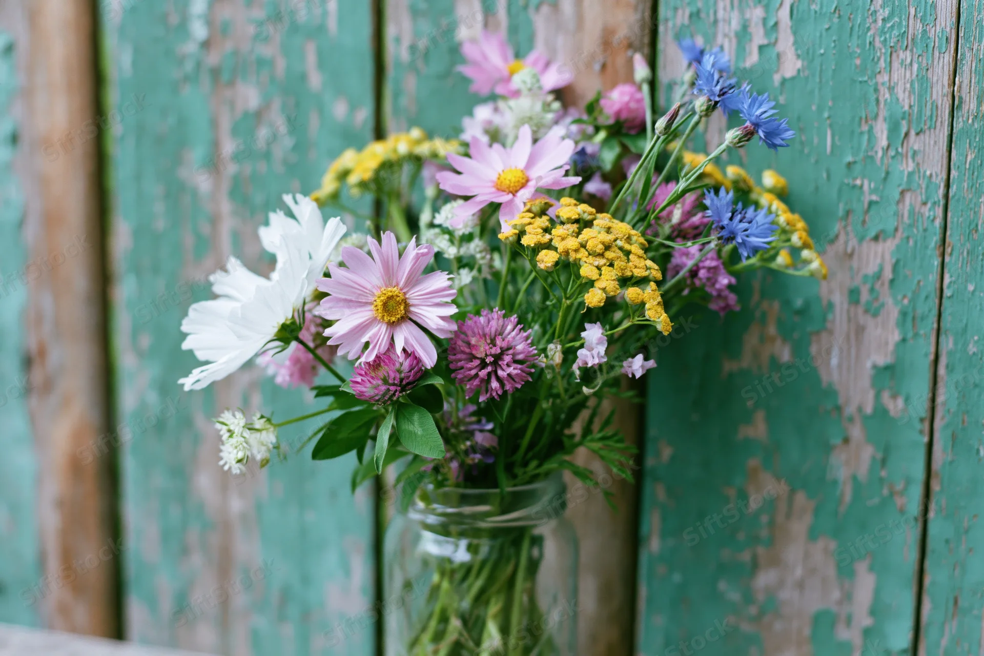 Loose wildflower bouquet in a clear glass jar against weathered teal wooden planks