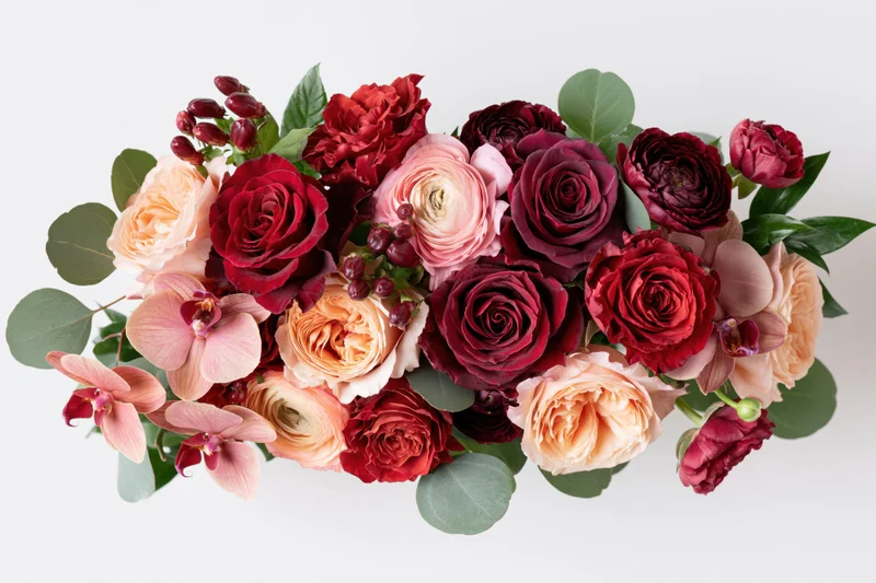 Horizontal mixed flower bouquet with roses, orchids, and greenery on white background