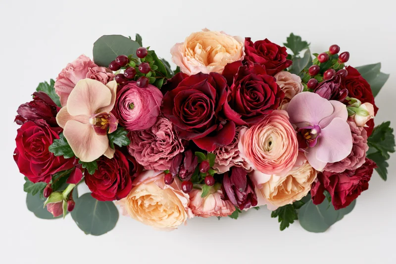 Horizontal mixed flower bouquet with roses, ranunculus, orchids and eucalyptus on white background