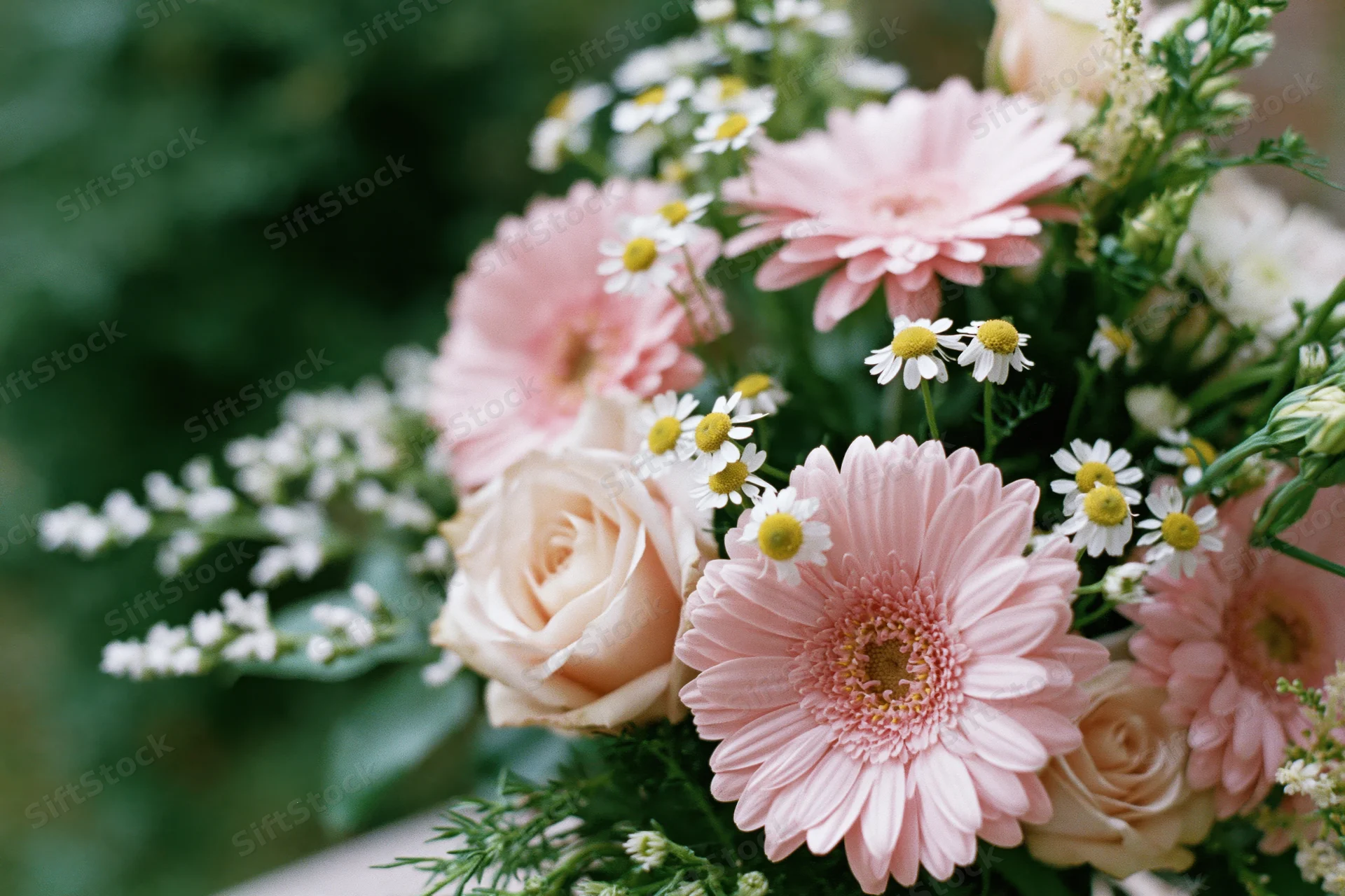 Mixed bouquet of pink roses, gerbera daisies and white daisies arranged with greenery on a surface