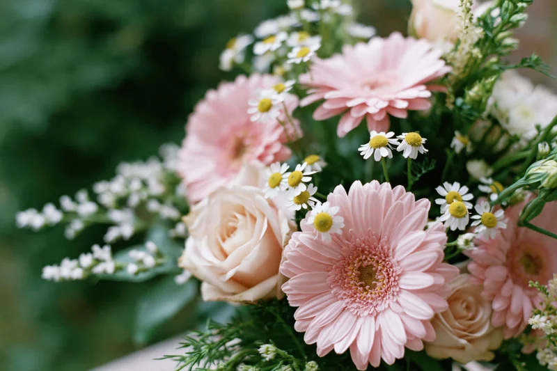 Mixed bouquet of pink roses, gerbera daisies and white daisies arranged with greenery on a surface